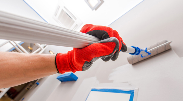 Close-up of painter using a roller brush to apply paint to siding or exterior wall in Orlando, FL