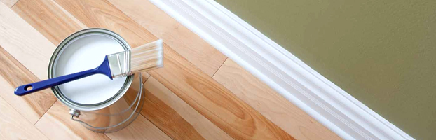 Paintbrush resting on a white paint can near a freshly painted baseboard in Orlando, FL home
