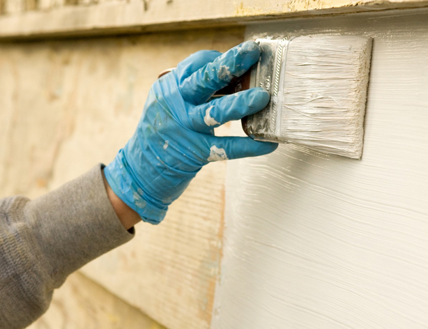 Exterior house painting with a brush applying white paint to wood siding in Orlando, FL